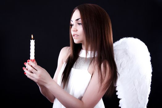 Beautiful young angel with a candle over black background