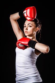 Beautiful young woman in a red boxing gloves over black background