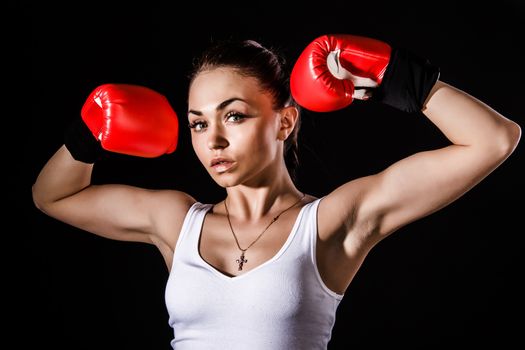 Beautiful young woman in a red boxing gloves over black background