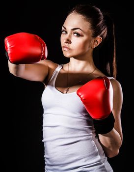 Beautiful young woman in a red boxing gloves over black background