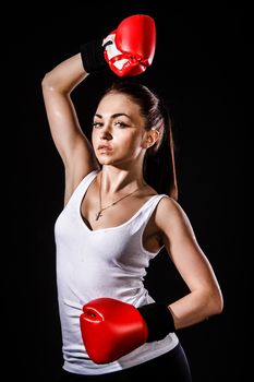 Beautiful young woman in a red boxing gloves over black background