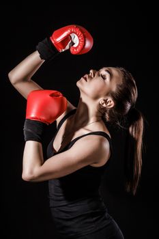 Beautiful young woman in a red boxing gloves over black background