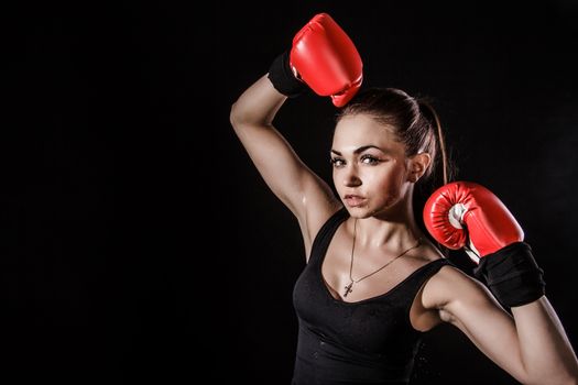 Beautiful young woman in a red boxing gloves over black background