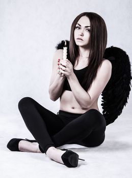 Beautiful young woman in a costume of the fallen angel holding a candle over grey background