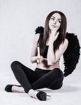 Beautiful young woman in a costume of the fallen angel holding a candle over grey background