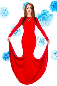 Beautiful young woman in a long red evening dress at the background of the cyan flowers