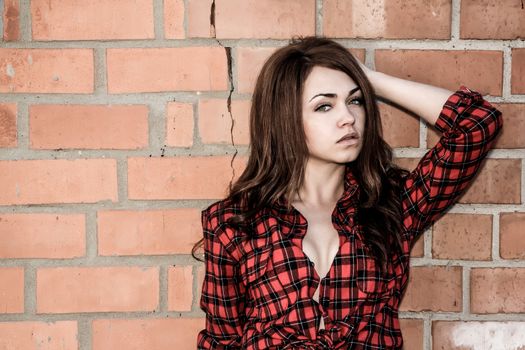 Beautiful young woman in a checked shirt at the background of the brick wall