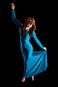 Gorgeous young lady dancing in a long green evening dress over black background