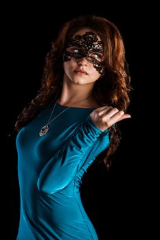 Beautiful young woman in a black mask and a green dress over black background