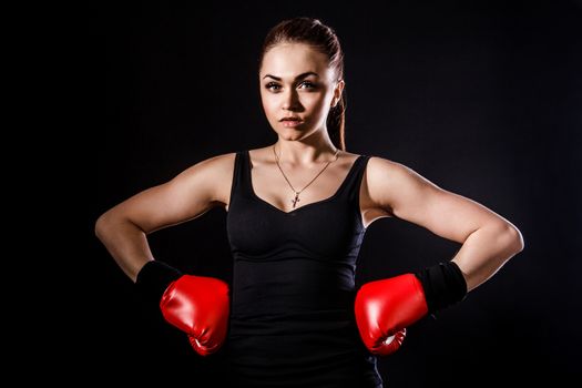 Beautiful young woman in a red boxing gloves over black background