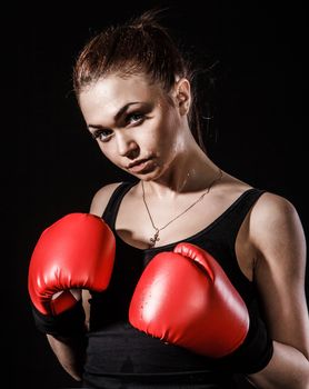 Beautiful young woman in a red boxing gloves over black background