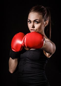 Beautiful young woman in a red boxing gloves over black background