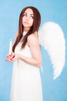 Beautiful young angel holding a candle over blue background