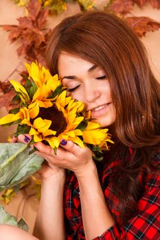 Cute young woman holding the sunflowers at the background of maple leaves