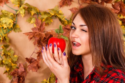 Cute young woman holding an apple at the background of maple leaves