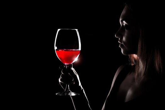 Beautiful young woman holding the glass of a red wine in darkness