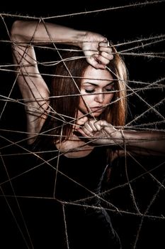 Beautiful young woman behind the interlaced ropes over black background