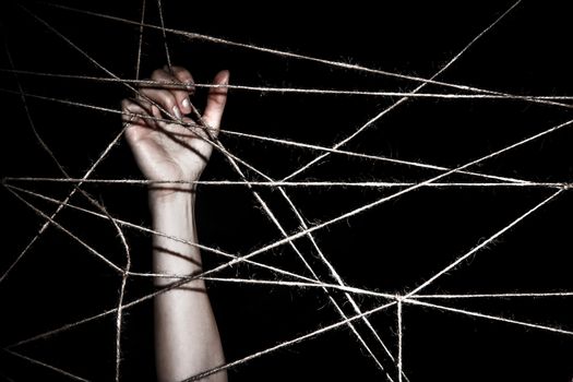 Slim hand behind the interlaced ropes over black background