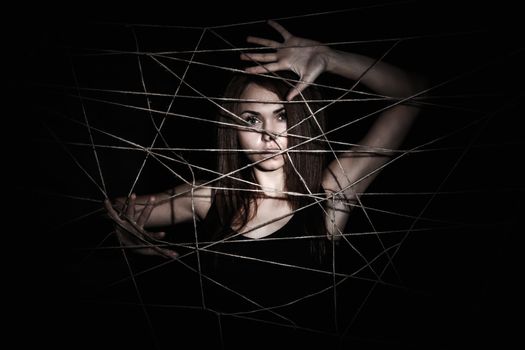 Beautiful young woman behind the net of ropes over black background