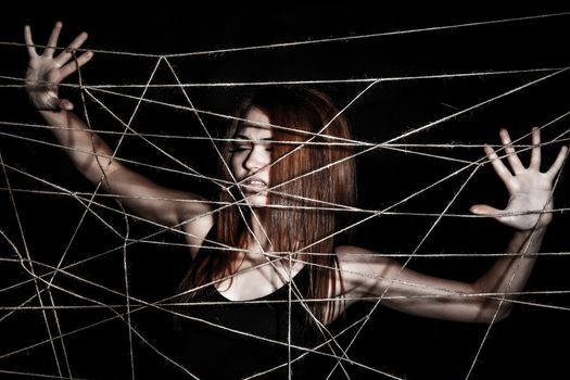 Beautiful young woman behind the interlaced ropes over black background