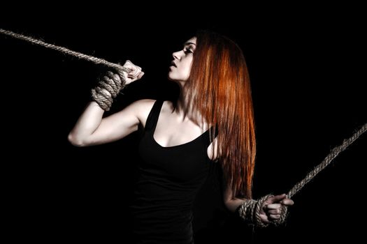 Beautiful young woman with bright red hair and tied arms over black background