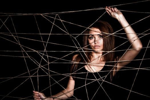 Beautiful young woman behind the net of ropes over black background