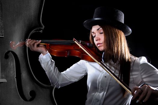 Beautiful young violinist playing a violin over black background