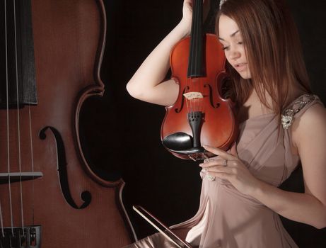 Pretty young woman holding a violin over black background
