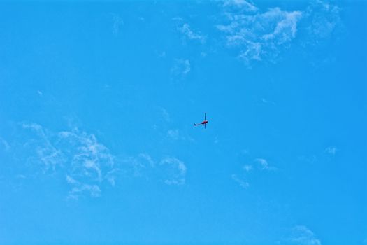 Small red helicopter hovering on blue sky