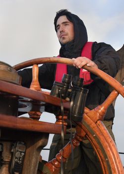 Young sailor on a ship's deck behind a steering wheel