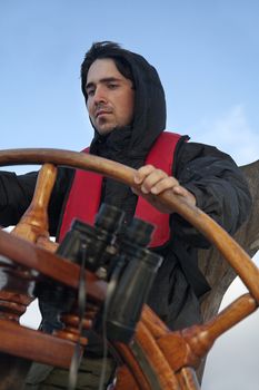 Young sailor on a ship's deck behind a steering wheel