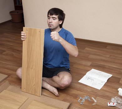 Young man sitting on floor assembling flatpack closet