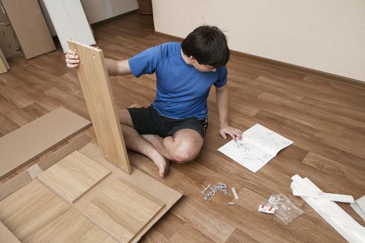 Young man puzzled about assembling flatpack closet