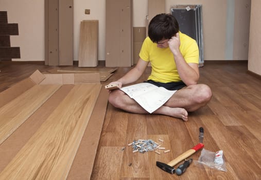 Young man sitting on floor assembling flatpack closet