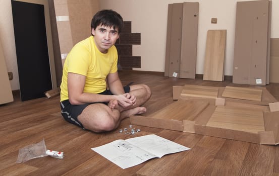 Young man sitting on floor assembling flatpack closet