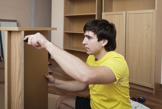 Young man sitting on floor assembling flatpack closet