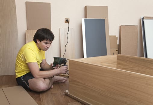 Young man sitting on floor assembling flatpack closet