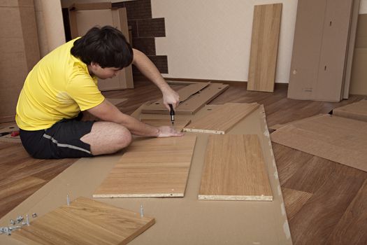 Young man sitting on floor assembling flatpack closet