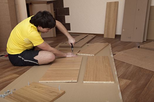 Young man sitting on floor assembling flatpack closet