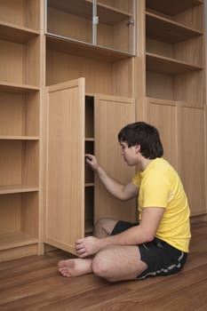 Young man sitting on floor assembling flatpack closet