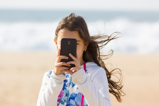 Cute Girl taking photo with cellphone on the beach, sea background.