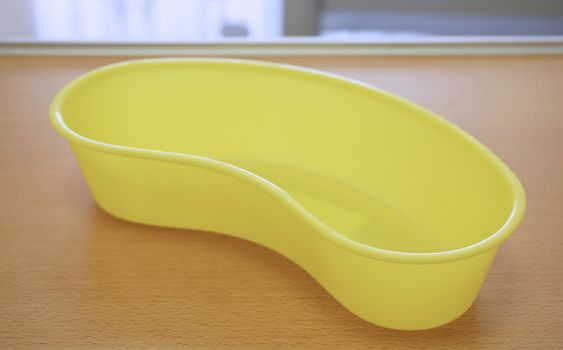 Yellow colour of plastic medical basin placed on wood table in patient room.