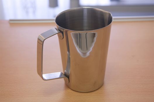 Stainless mug or medical jug placed on over bed table in patient room.