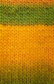 Length of stocking stitch knitting in green and yellow yarn as an abstract background texture