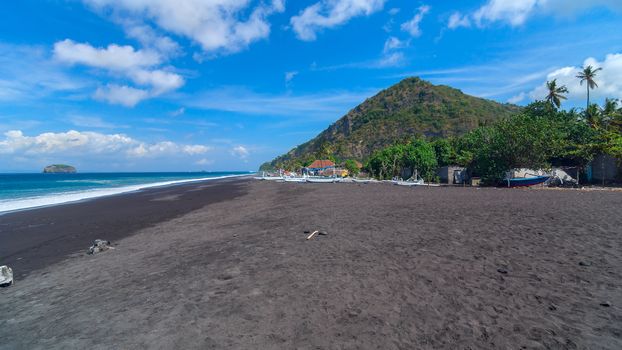 Junks on the beach of black sand on the island of Bali in Indonesia. Summer sunny day.