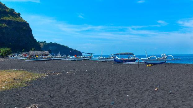 Boats on the beach of black sand on the island of Bali in Indonesia. Summer sunny day.