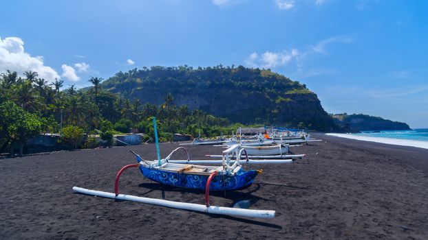 Junk on the beach of black sand on the island of Bali in Indonesia. Summer sunny day.