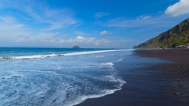 The beach with black volcanic sand on the island of Bali in Indonesia on a sunny summer day.