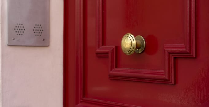 Shiny brass metal doorknob on red wooden entrance door