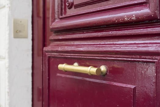 Old brass door handle on sturdy old textured maroon red wooden door